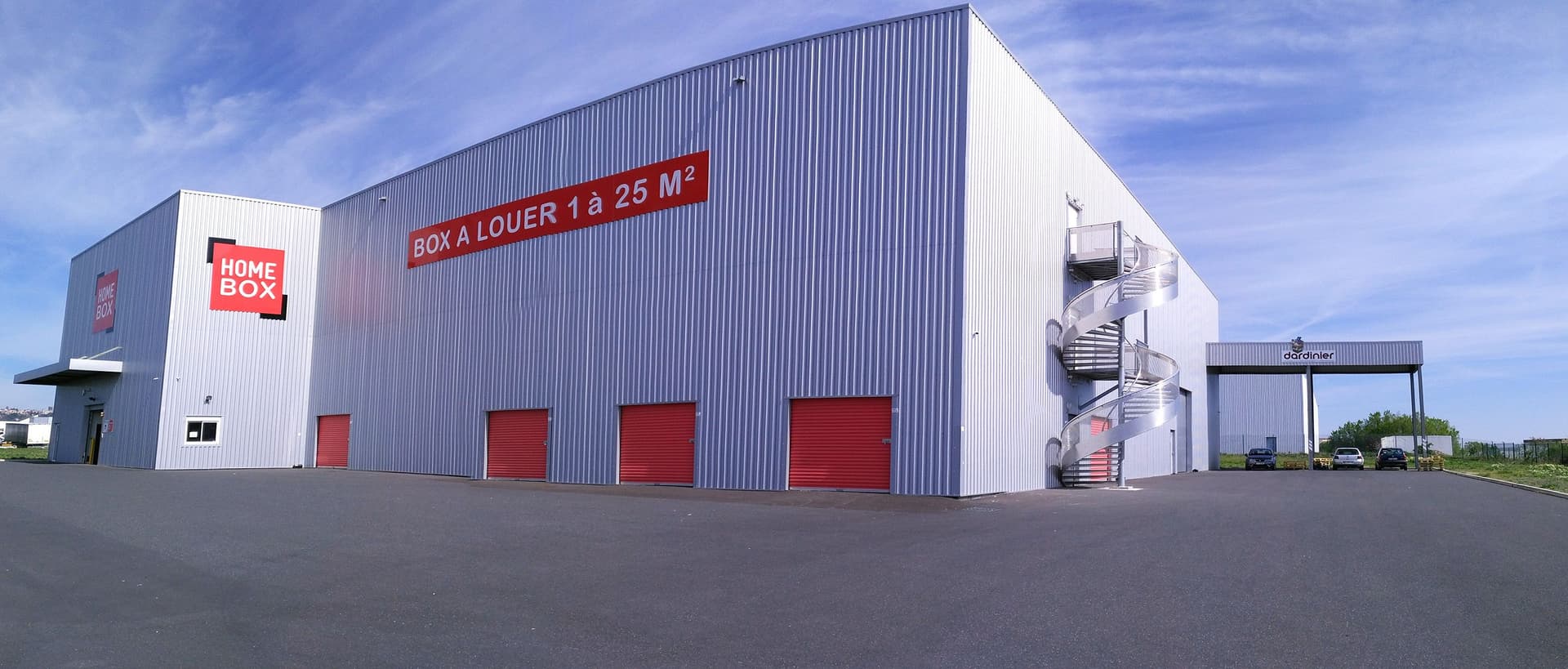 Vue extérieure du bâtiment HOMEBOX Cébazat avec plusieurs box accessibles et large parking.