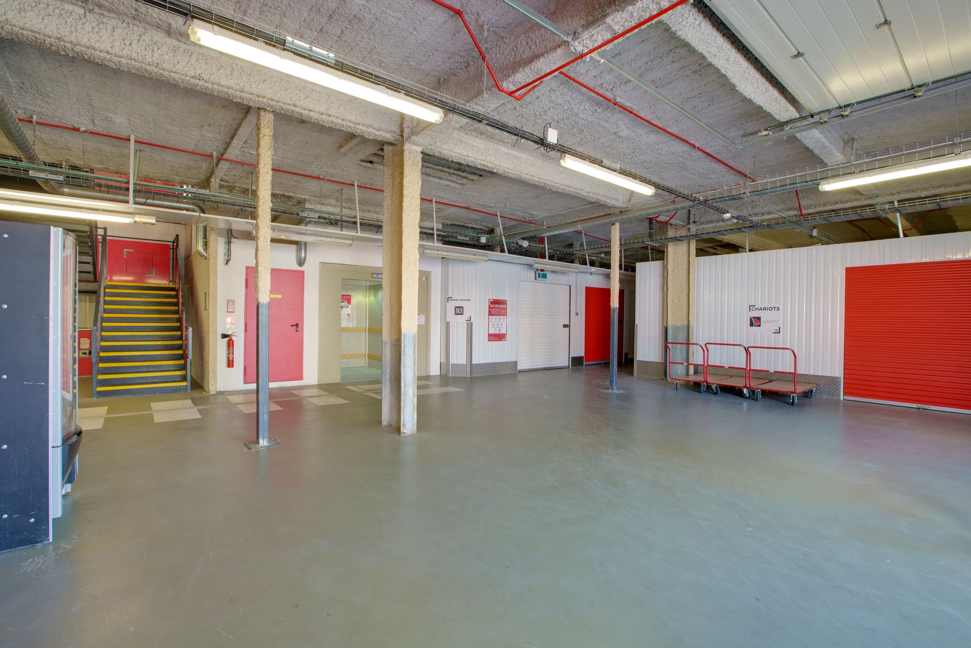 Espace de déchargement intérieur du centre HOMEBOX Grenoble, avec portes roulantes rouges et ascenseur.